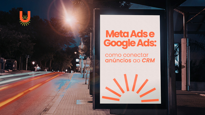 Painel publicitário iluminado em ponto de ônibus à noite, com rua urbana, árvores e rastros de luz dos carros em movimento.