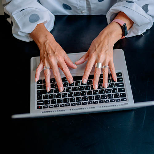 Mãos digitando em notebook sobre mesa escura, indicando atividade de trabalho ou uso de tecnologia.