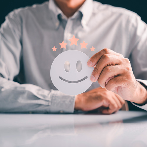 Pessoa segura ícone de rosto sorridente com estrelas acima, simbolizando satisfação e avaliação positiva de serviço.