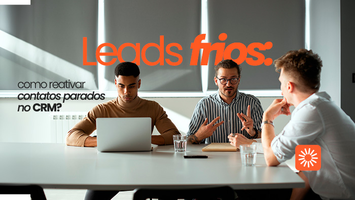 Grupo em reunião de trabalho, com pessoas conversando e usando notebook em mesa com copos de água.